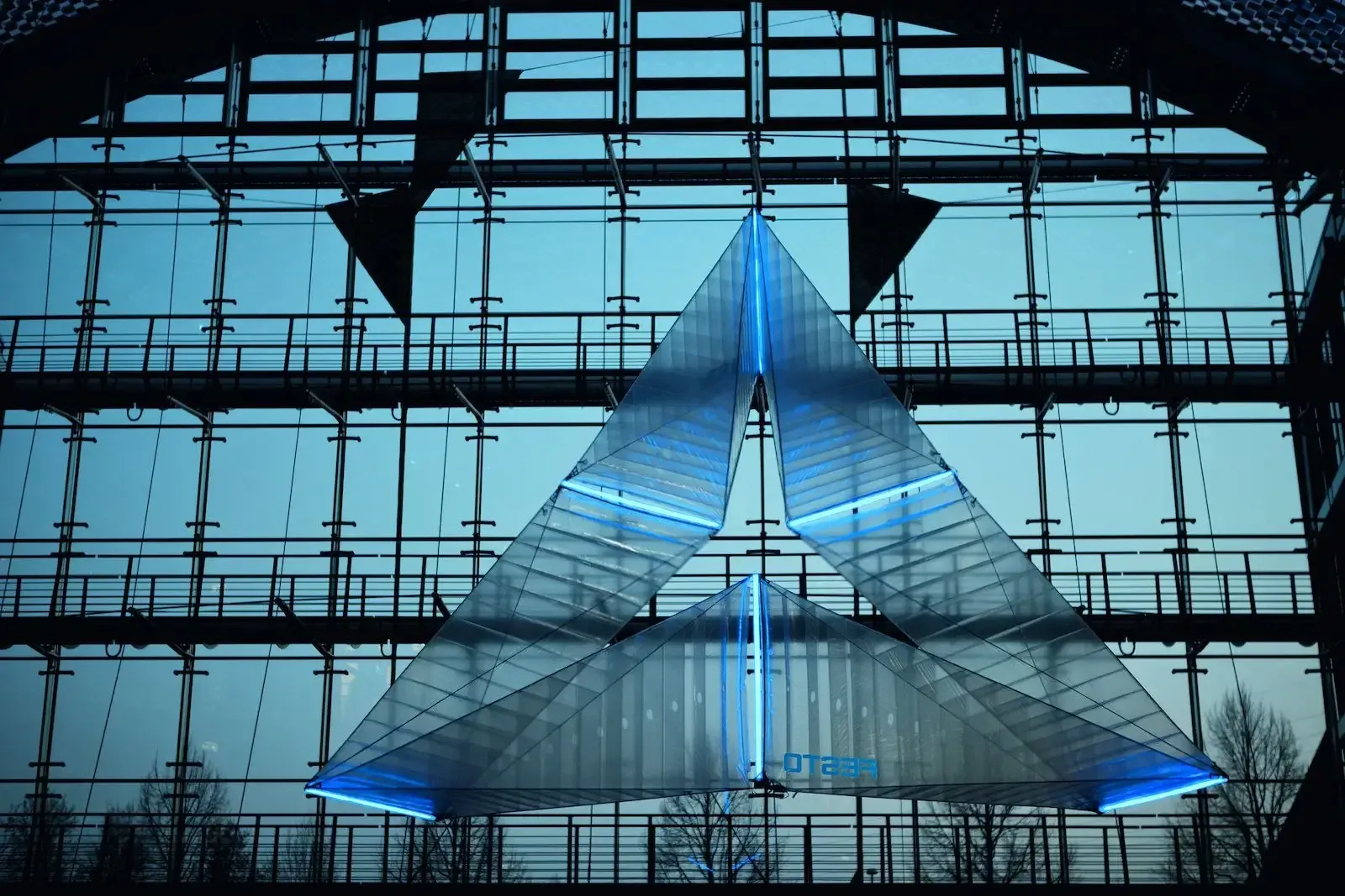 The SmartInversion flying geometric object glowing blue in a glass hall