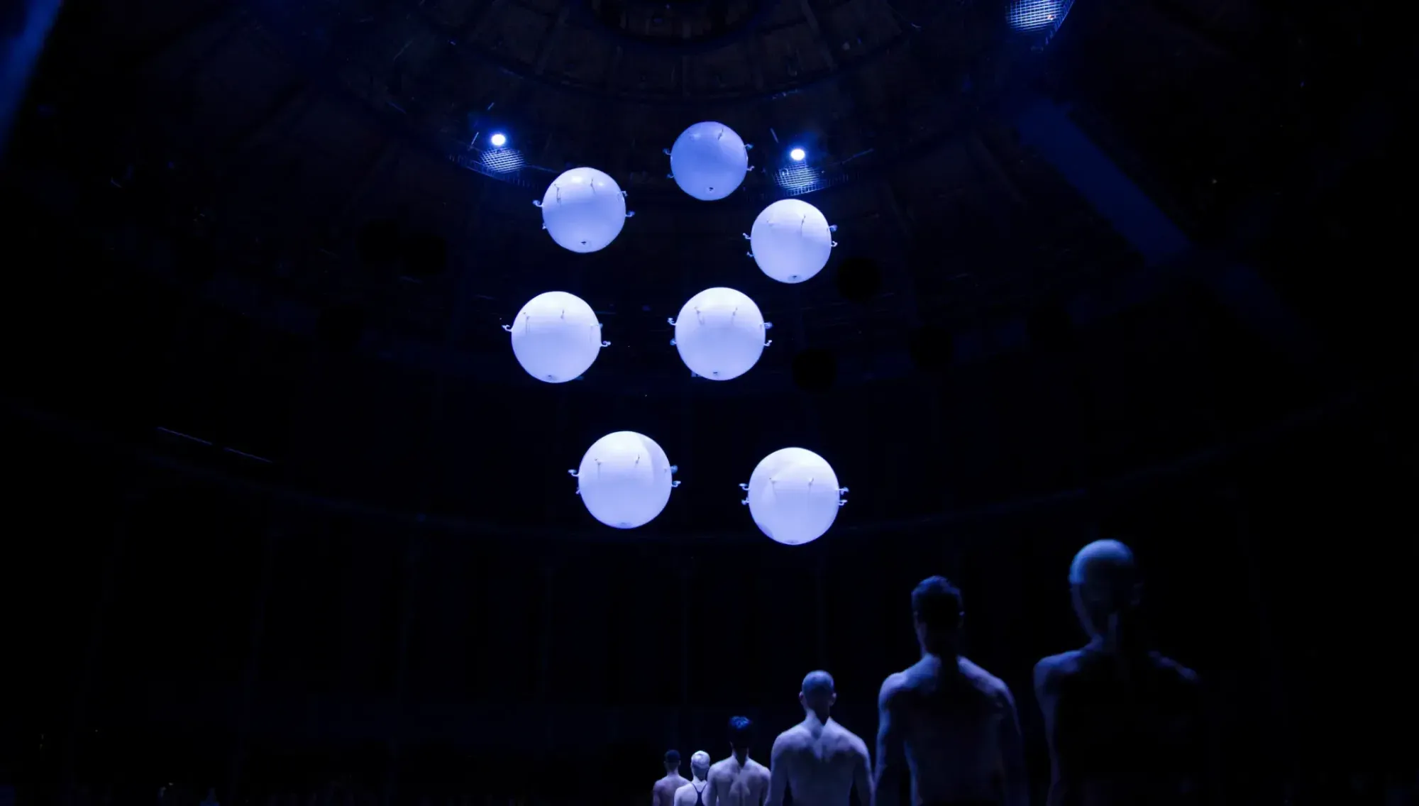 Glowing white orbs hovering above dancers in darkness at the Roundhouse, London